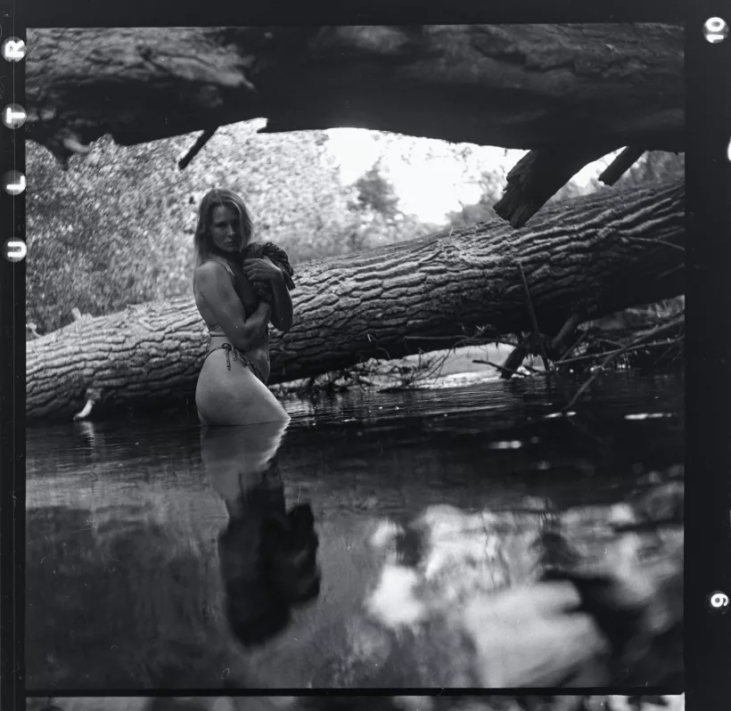 Analoges Schwarz-Weiß-Portrait einer Frau am Ufer eines Waldteichs neben einem Baumstamm