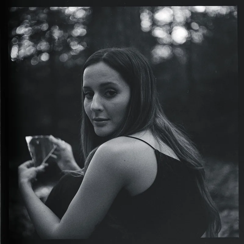 Analoges Schwarzweiß-Portrait einer Frau mit langen Haaren vor einem unscharfen Waldhintergrund.