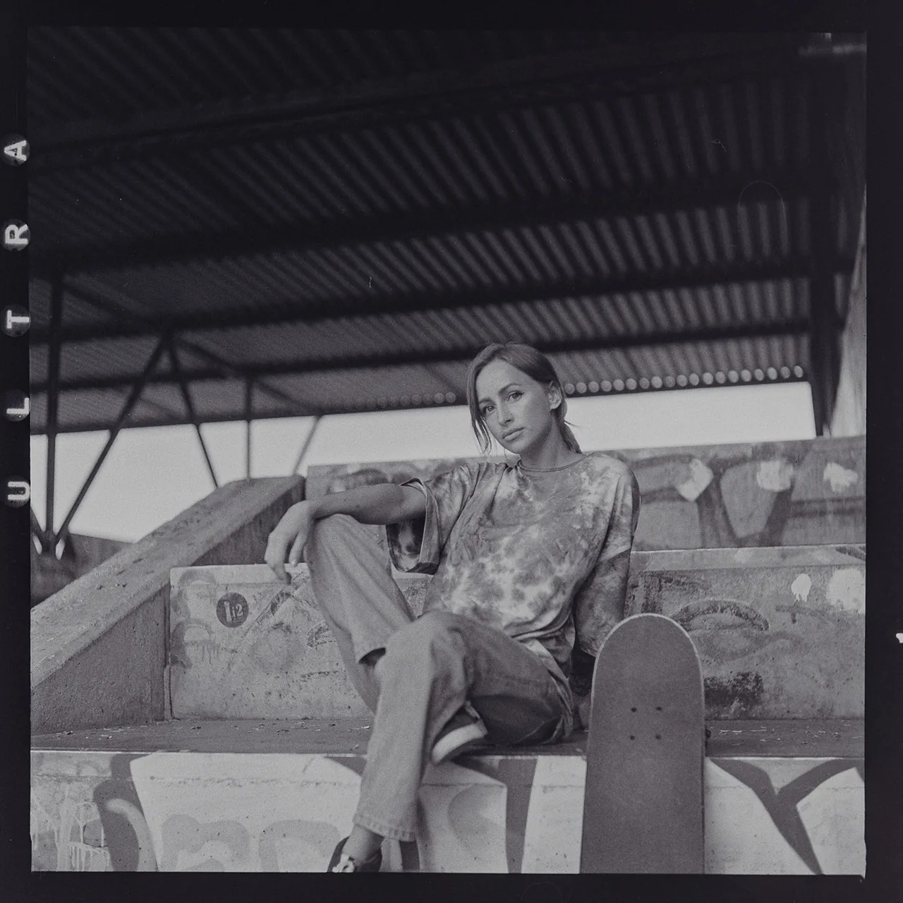Analoges Schwarzweiß-Portrait einer Frau, die neben einem Skateboard auf Betonstufen sitzt.