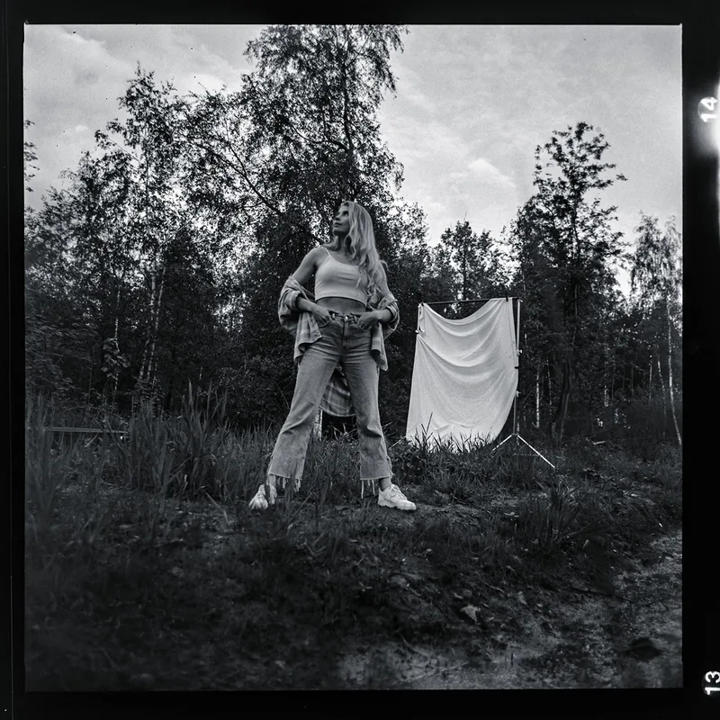 Analoges Schwarz-Weiß-Portrait einer Frau in Jeans vor einem weißen Tuch im Wald