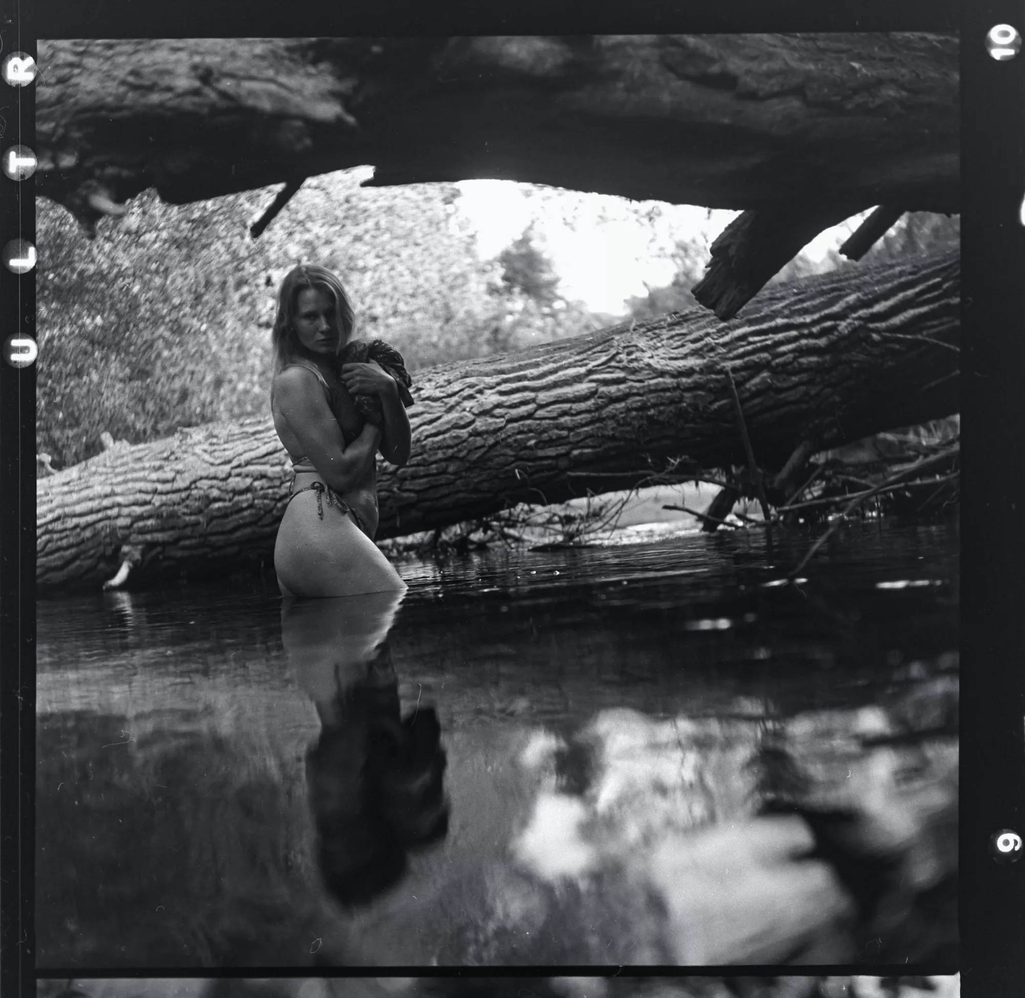 Analoges Schwarzweißportrait einer Frau im Wasser neben einem liegenden Baumstamm