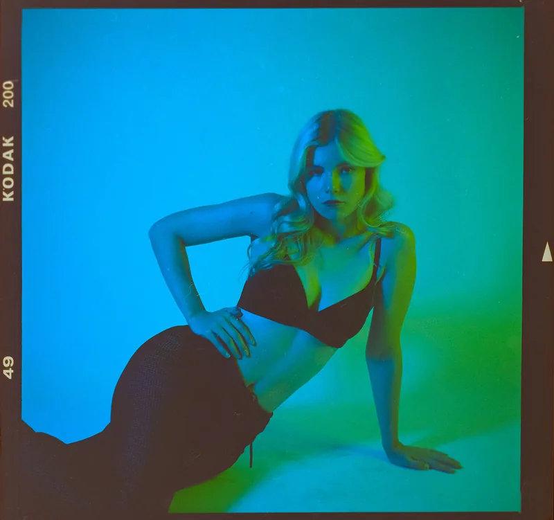 Analoges Studioportrait einer Frau mit blonden Haaren in blau-grüner Beleuchtung.