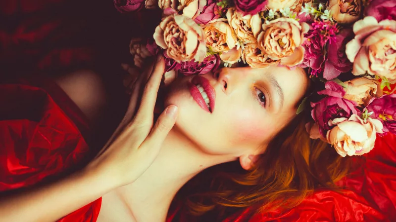 Beauty-Portrait einer Frau mit einem opulenten Blumenkranz aus rosa und cremefarbenen Blüten.