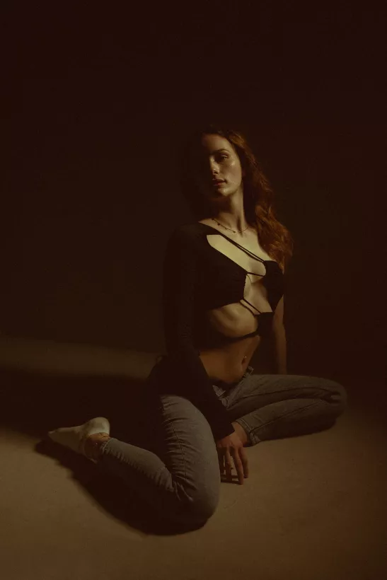 Boudoirfoto einer Frau in schwarzem Cutout-Top und grauer Jeans