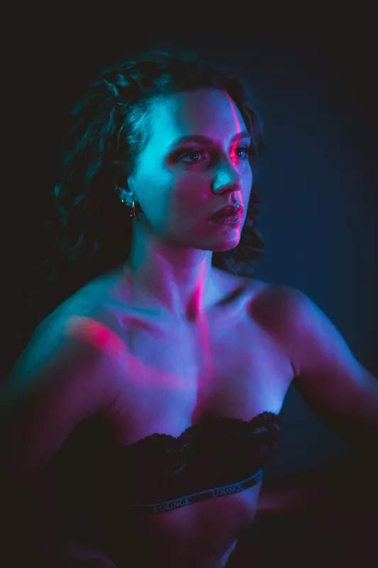 Boudoir-Portrait einer Frau mit welligem Haar in blauem und rotem Neonlicht
