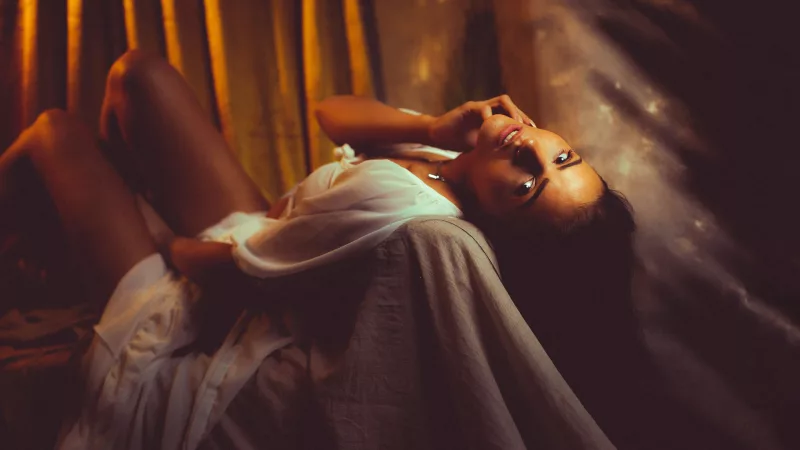 Boudoirfoto einer Frau in weißer Kleidung, die auf einem Bett liegt