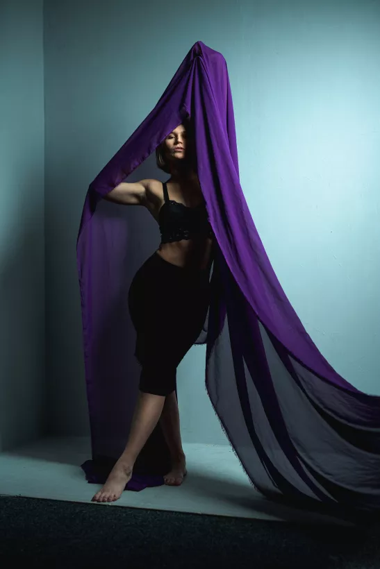 Boudoirfoto einer Frau in schwarzer Unterwäsche unter fließendem violettem Stoff