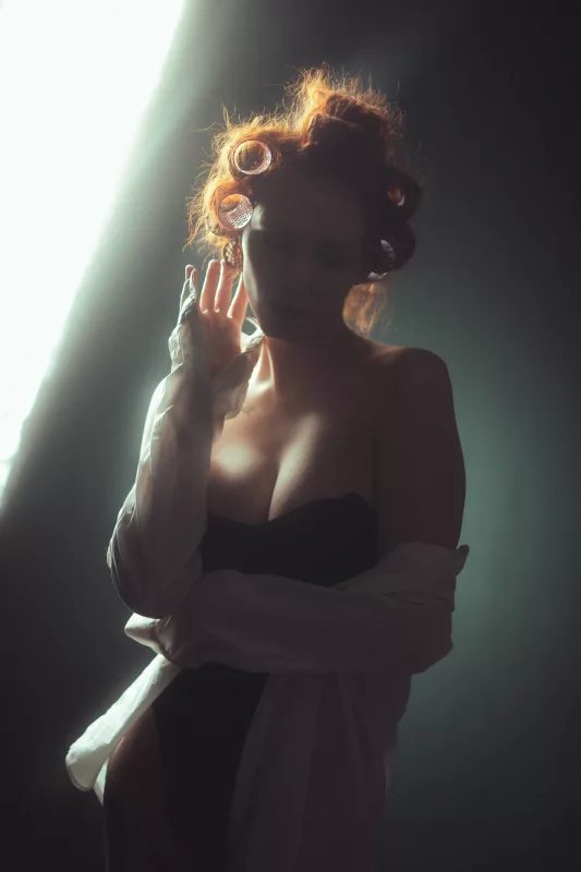 Boudoirportrait einer Frau mit Lockenwicklern in dramatischer Gegenlichtbeleuchtung.