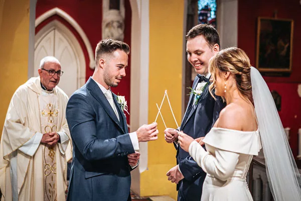 Braut und Bräutigam halten bei der Trauung ein goldenes Band in einer Kirche.