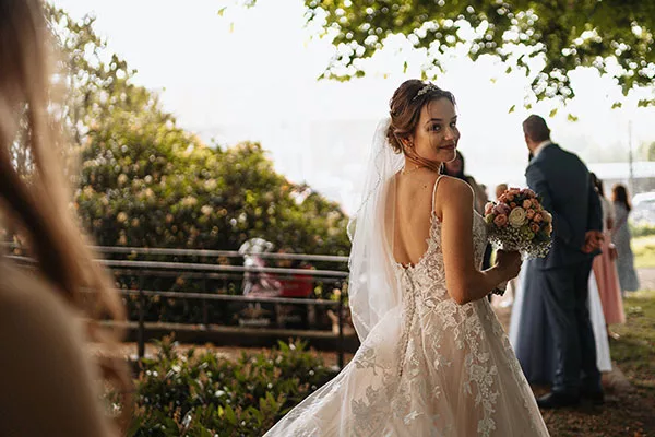 Braut im Hochzeitskleid mit Blumenstrauß beim Blick über die Schulter