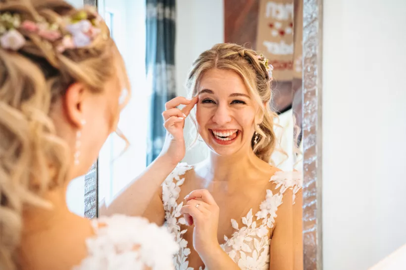 Lachende Braut mit Blumen im Haar beim Blick in den Spiegel