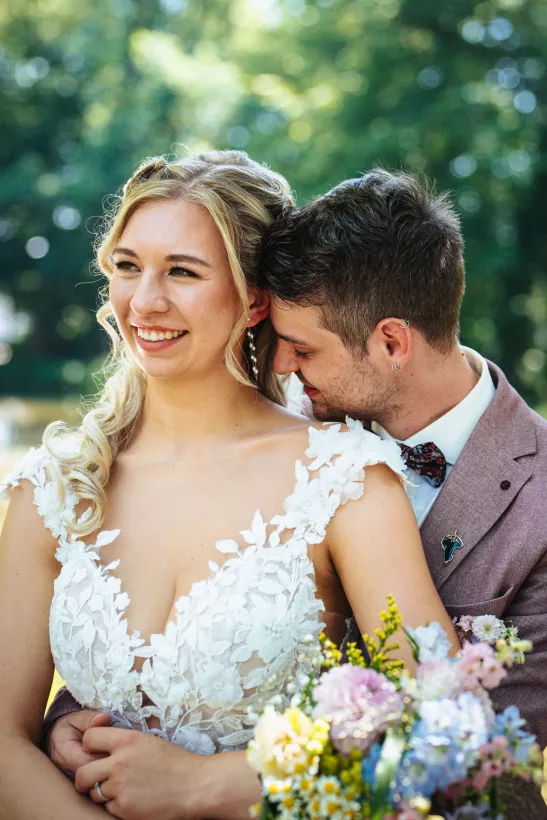 Lächelnde Braut im Spitzenkleid und Bräutigam bei einem Hochzeitsfoto im Grünen
