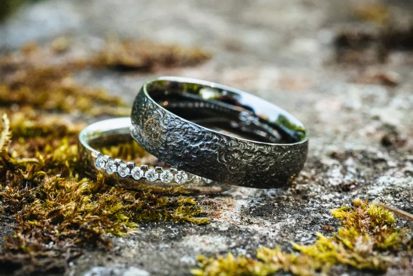Zwei Eheringe mit Textur und Diamanten auf bemoostem Stein