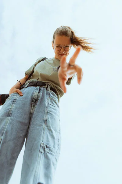 Eventfoto einer Frau mit Brille und hellgrünem T-Shirt in weiten Jeans, die nach der Kamera greift.