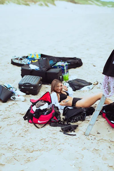 Eventfoto einer Frau, die inmitten von Taschen und Ausrüstung am Strand liegt.