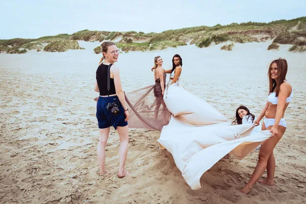Eventfoto einer Gruppe von Frauen am Strand mit einem großen, fließenden weißen Stoff.
