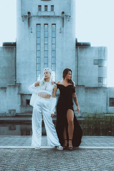 Eventfoto von zwei Frauen in eleganter weißer und schwarzer Kleidung vor einem imposanten Betongebäude.