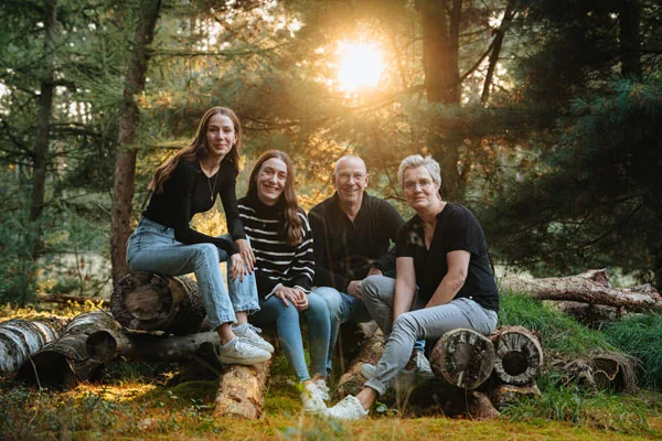 Warmes Familienfoto einer Gruppe auf Baumstämmen im sonnendurchfluteten Wald