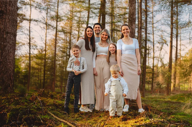 Familienfoto einer mehrköpfigen Familie in hellen, aufeinander abgestimmten Outfits im Wald.