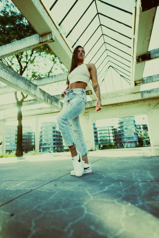 Fashion-Portrait einer Frau in weißem Crop-Top und Jeans unter moderner Architektur