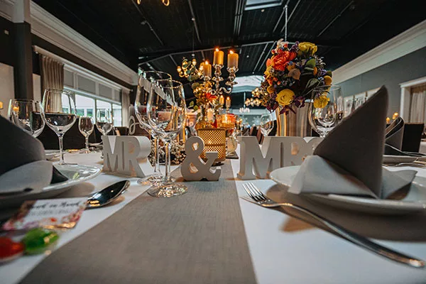 Festlich gedeckter Hochzeitstisch mit „MR & MRS“ Schriftzug, Weingläsern und Blumenarrangements.