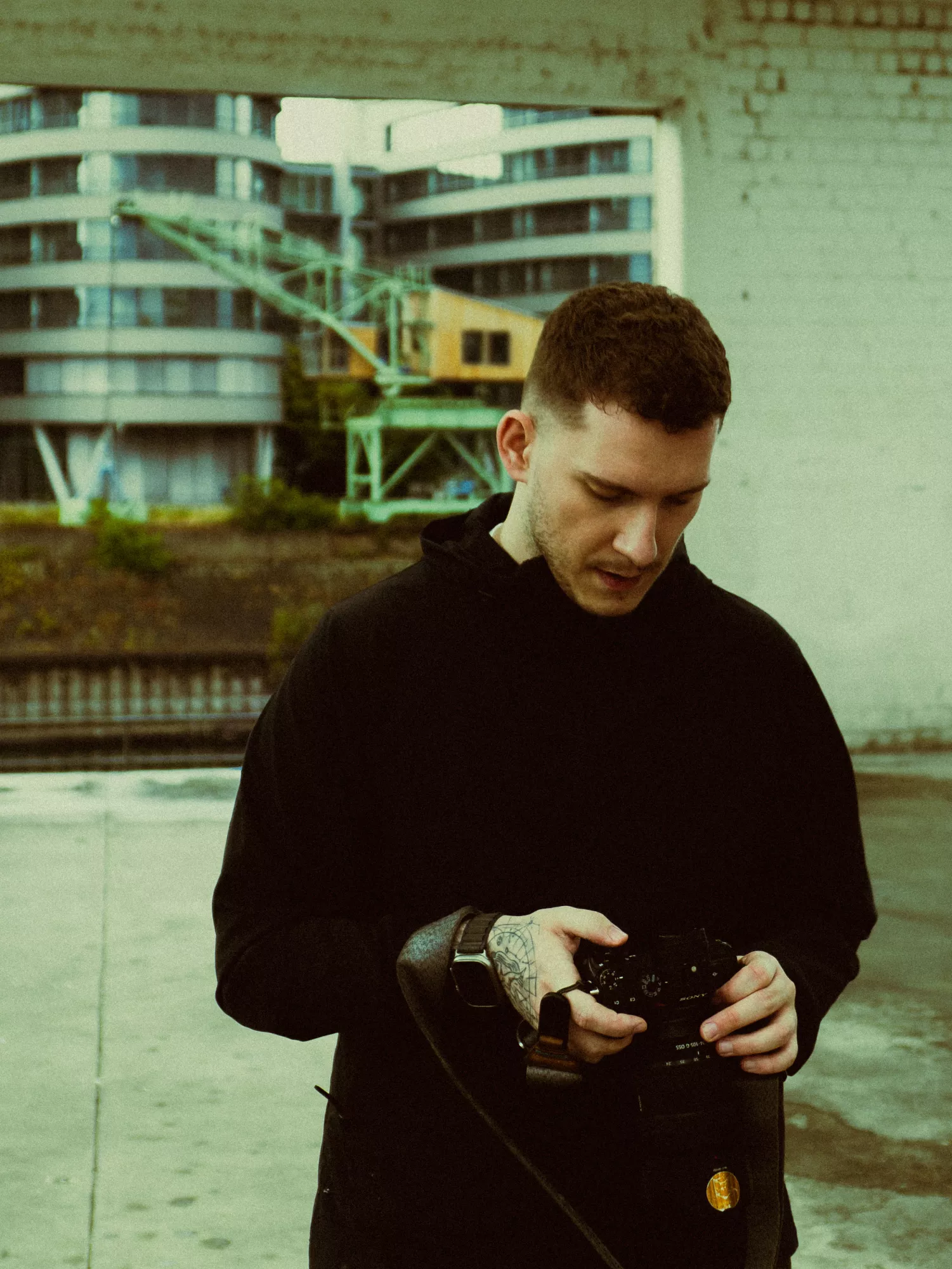 Mann in schwarzem Hoodie blickt konzentriert auf seine Kamera vor urbaner Kulisse