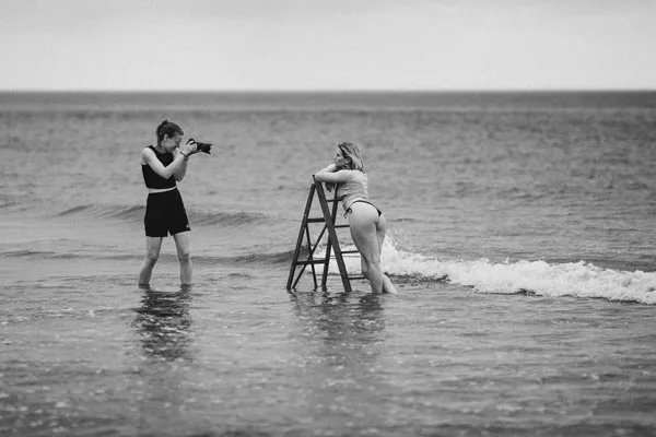 Eine Fotografin fotografiert eine Frau auf einer Holzleiter im Meer.