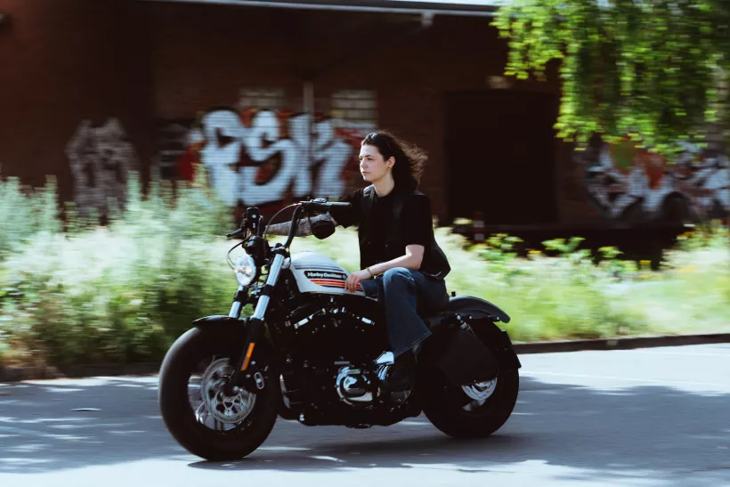 Streetfotografie einer Frau auf einem Motorrad vor einer Graffiti-Wand in der Stadt.