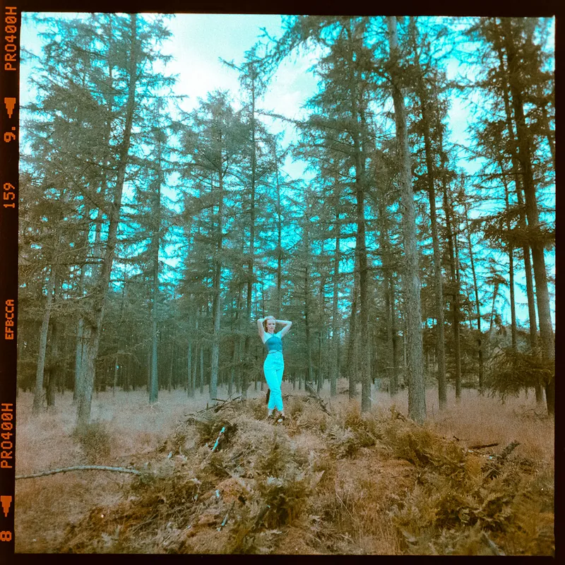 Frau in blauem Outfit zwischen hohen, schlanken Bäumen im Wald.