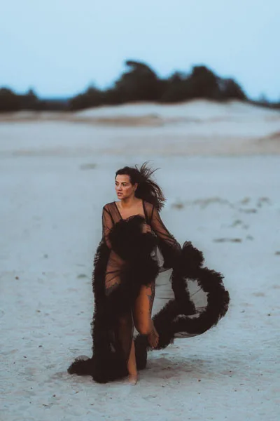 Frau in einem fließenden schwarzen Tüllkleid am sand