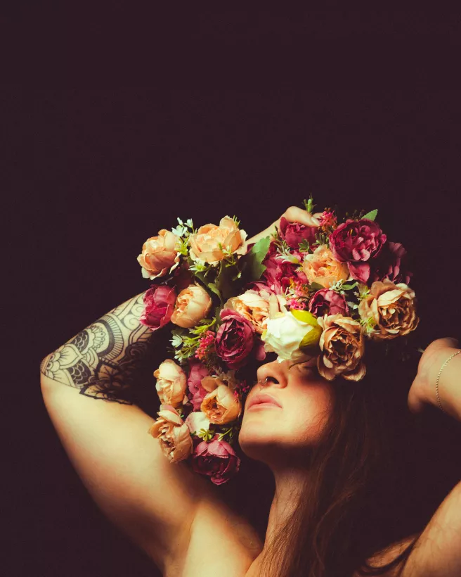 Künstlerisches Studioportrait einer Frau mit farbenfrohem Blumenschmuck vor dem Gesicht