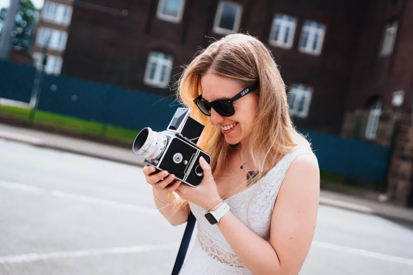 Lächelnde Frau mit Sonnenbrille und klassischer Analogkamera