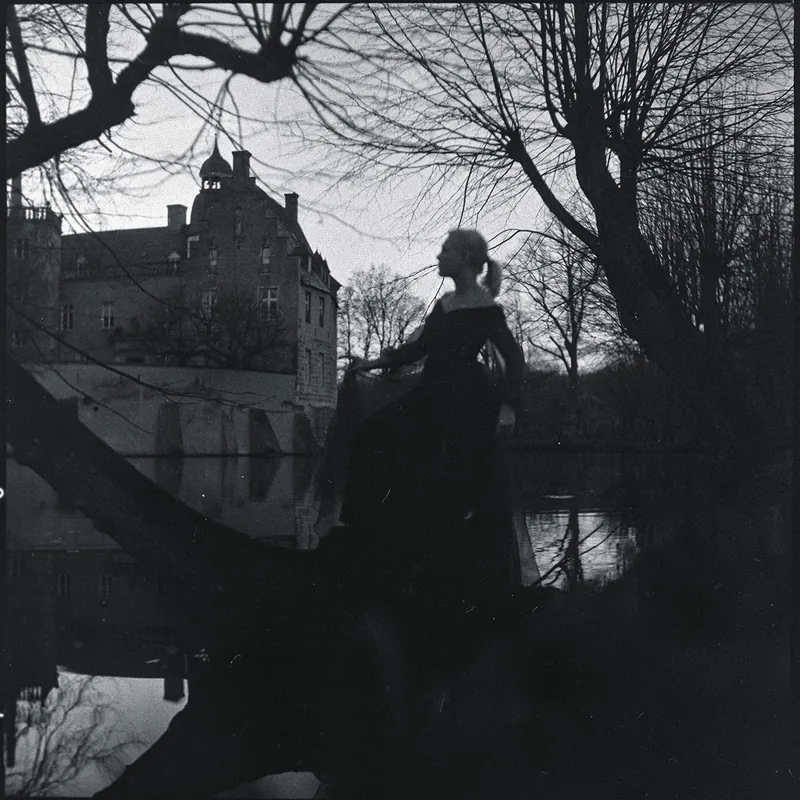 Silhouette einer Frau vor einem Schloss und kahlen Bäumen am Wasser