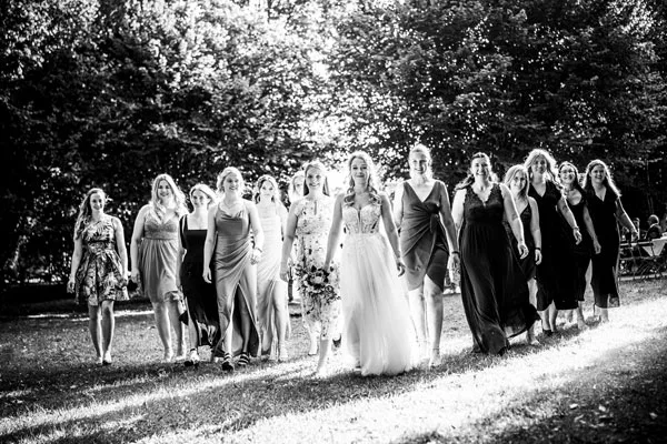 Eine Gruppe lächelnder Brautjungfern in eleganten Kleidern bei einem Schwarz-Weiß-Hochzeitsfoto im Wald.
