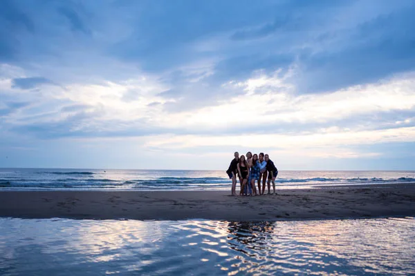 Gruppe von Menschen am Strand unter einem weiten, bewölkten Himmel bei Dämmerung.
