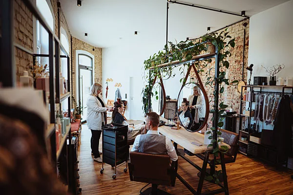 Heller Friseursalon mit Backsteinwänden, runden Spiegeln und hängenden Pflanzen.