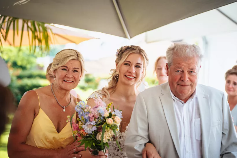 Hochzeitsfoto einer Braut mit Blumenstrauß und zwei Begleitpersonen
