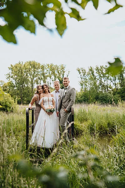 Hochzeitsfoto eines Brautpaares mit Begleitung auf einer grünen Wiese vor Bäumen