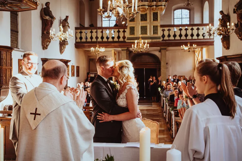 Hochzeitsfoto eines Brautpaares beim Kuss während der Zeremonie in einer Kirche.