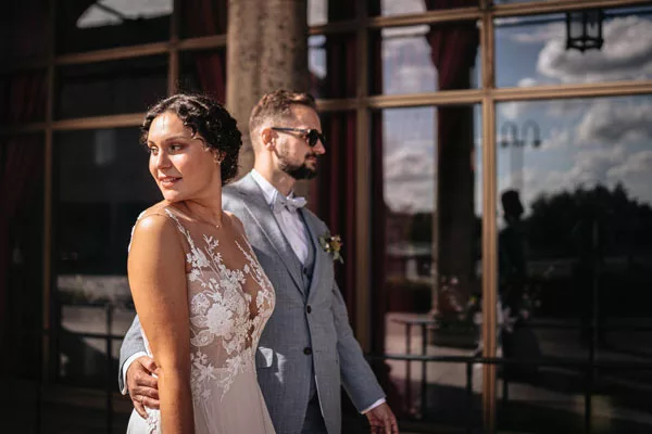 Braut in weißem Spitzenkleid und Bräutigam im hellblauen Anzug bei einem Hochzeitsfoto