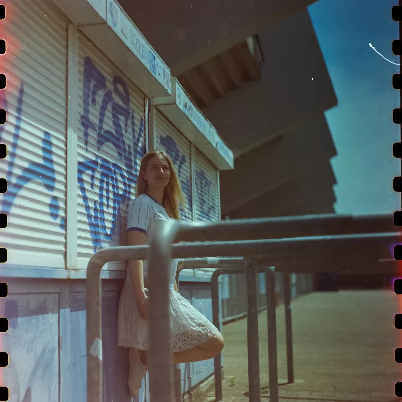 Analoges Portrait einer jungen Frau mit blondem Haar in einem weißen Spitzenkleid vor einer Wand mit blauem Graffiti