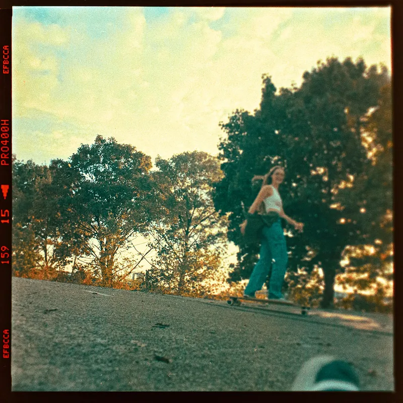 Junge Frau auf einem Skateboard vor einer Kulisse aus Bäumen