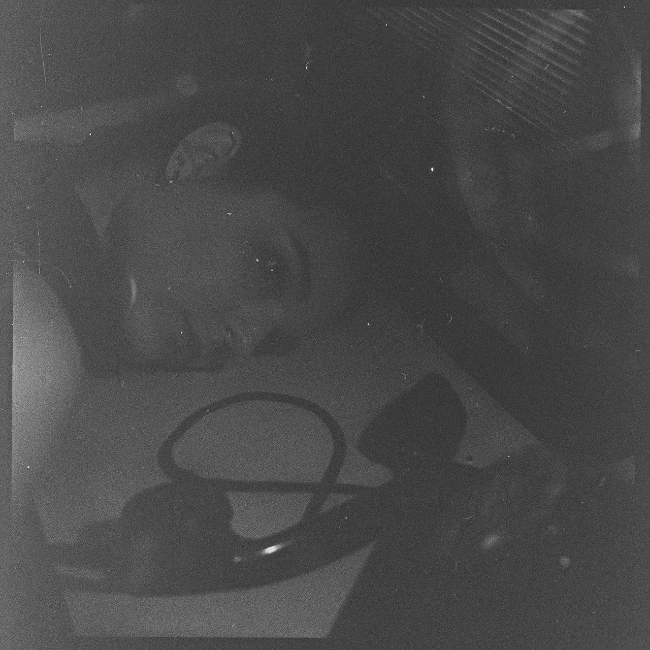 Körniges, analoges Porträt einer Person im Halbschatten mit einem unscharfer Telefonhörer im Vordergrund.