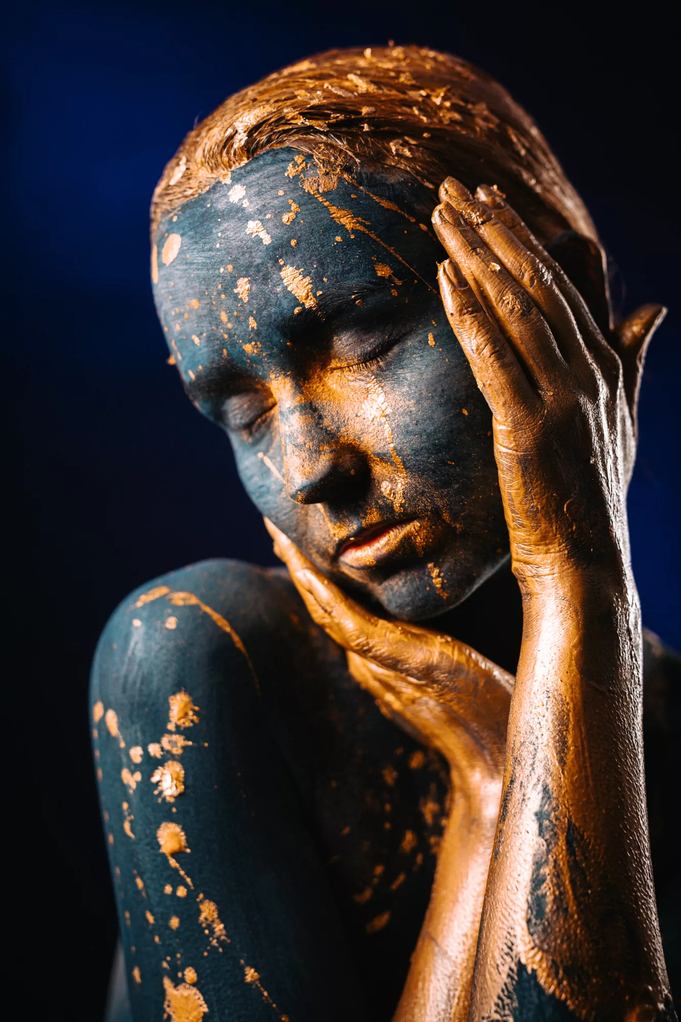 Künstlerisches Porträt mit blauem und goldenem Bodypaint auf Gesicht und Händen.