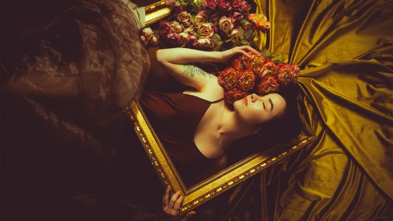 Künstlerisches Portrait einer Frau inmitten von Rosen und goldenem Stoff in einem Prunkrahmen.