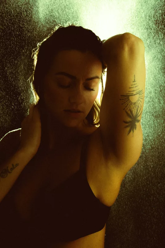 Künstlerisches Portrait einer Frau mit Sonnen-Tattoo am Oberarm im warmen Gegenlicht.