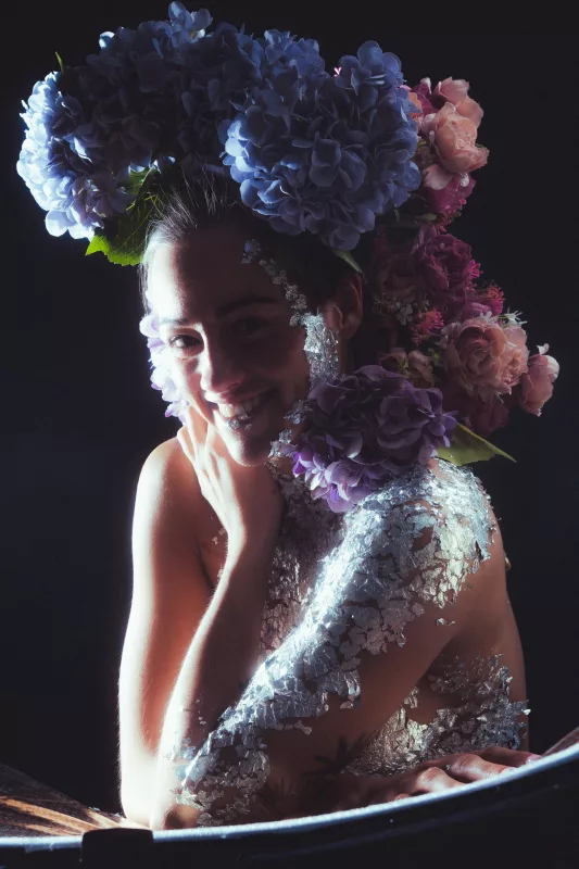 Künstlerisches Portrait einer lächelnden Frau mit opulentem Kopfschmuck aus blauen und rosa Hortensien.