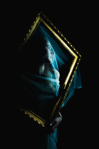 Künstlerisches Portrait einer Person hinter einem verzierten Goldrahmen unter einem blauen, transparenten Schleier.