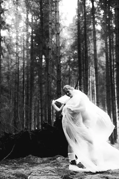Künstlerisches Schwarz-Weiß-Portrait einer Person in fließendem, hellem Gewand im Wald.