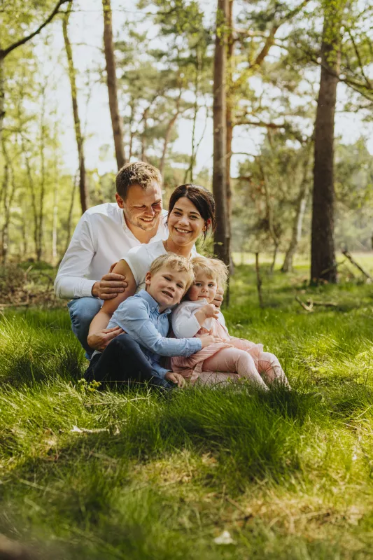 Lachende Familie sitzt gemeinsam auf einer Wiese im sonnigen Wald.